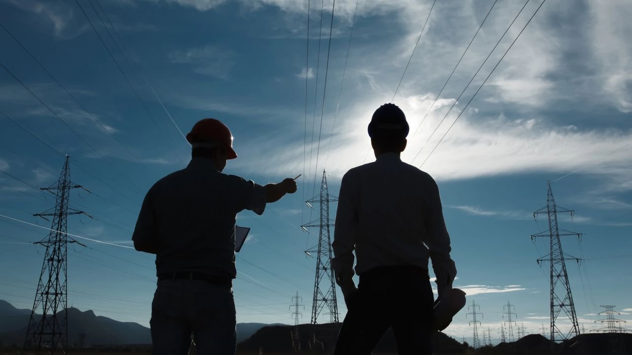 Dos profesionales de la ingeniería observando una línea de alta tensión al atardecer